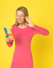 Attractive Happy Blond Woman In Red Dress Using Tablet Pc Holding In Hand For Videocall Conversation, Blogging For Social Media Gesturing With Hand Isolated On Yellow Background.