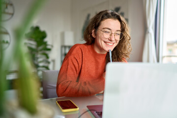 happy young woman using laptop sitting at desk writing notes while watching webinar, studying online