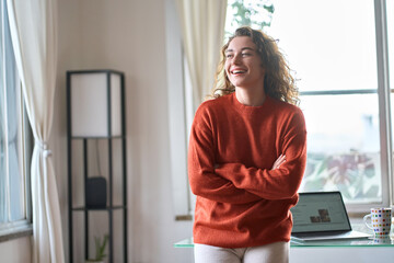 Wall Mural - Happy charming smiling confident young adult woman laughing standing in modern cozy apartment interior. Positive pretty lady wearing sweater feeling cheerful looking away at home in living room.