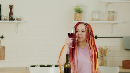 Wall Mural - Young woman with bright long dreadlocks drinking wine from glass in kitchen.