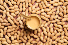 Peanut Butter In The Center Of The Image Photographed From Above. Groundnut In The Shell Around It. A Spoon Is In The Glass.