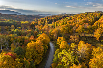 Autumn in New England with trees in full display of red and yellow, a gravel path and distant hills and mountains under a cloudy sky, Windsor, Vermont