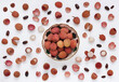 Lychee fruits in bowl on white background with scattered whole and peeled fruit, with seeds and peels. Top view. Decorative arranged lychees in flat lay style.