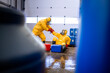 Accident in chemical factory, slippery floor, spilled chemicals. Worker in protection hazmat suit helping his colleague to stand up after the fall.