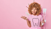 Confused Curly Haired Female Fairy Holds Wand Shrugs Shoulders Wears T Shirt Doesnt Know How To Prepare For Party Isolated Over Pink Background Empty Space For Your Advertising Content. Dental Care