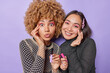 © wayhome.studio  - Horizontal shot of mixed race young women with bright makeup hold lip gloss apply makeup prepare for party look directly at camera wear jumpers isolated over purple background. Cosmetics concept