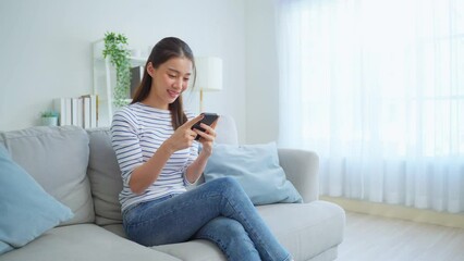 Wall Mural - Asian beautiful woman sit on sofa and talk on mobile phone in house.