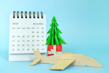 Selective Focus Of December 2022 Desk Calendar With Airplane Model And Christmas Tree On Blue Background. Christmas Season Vacation And Holiday Travel Concept.