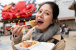 © PR Image Factory - smiling Asian Taiwanese female tourist looking at camera while enjoying eating yummy takoyaki octopus ball on chopsticks in Shinsekai area in Osaka Japan