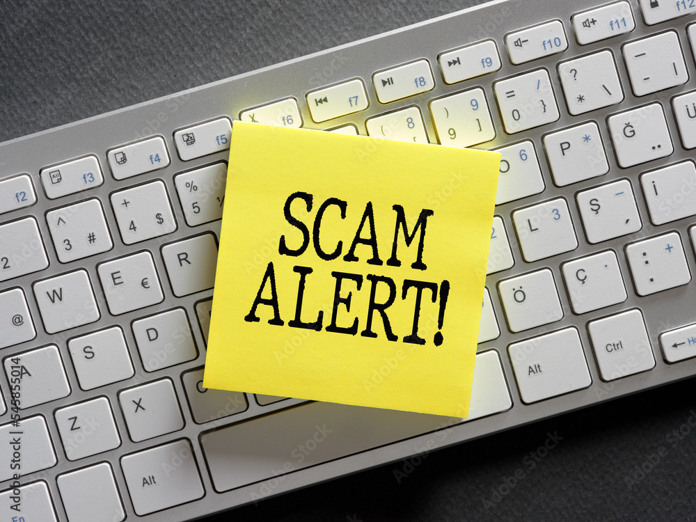 The word scam alert written on a sticky note paper on computer keyboard ...