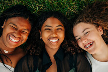 Portrait Of Happy Teenage Girls Laughing While Lying On Grass