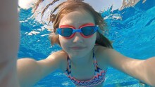 Cute Little Girl With Goggles Diving And Swimming Underwater In A Pool. Kid Taking Selfie In Water.