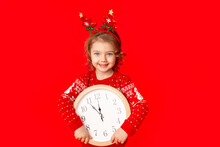 Child A Little Girl In Winter Clothes Holds A Watch On A Red Background. New Year's Concept, Space For Text