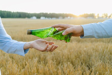 Hand of man passing crumpled plastic bottle to woman at field