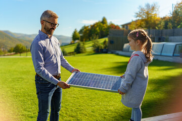 Wall Mural - Father with his little daughter catching sun at solar panel,charging at their backyard. Alternative energy, saving resources and sustainable lifestyle concept.