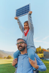 Wall Mural - Father with his little daughter on piggyback, catching sun at solar panel,charging it at their backyard. Alternative energy, saving resources and sustainable lifestyle concept.