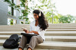 © Drobot Dean - Young woman using cellphone and headphones while studying outdoors