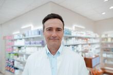 Smiling Pharmacist In Front Of Medicines Shelf At Pharmacy