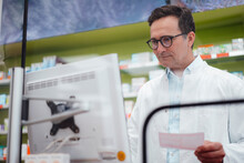 Pharmacist holding prescription searching medicine in database through computer at store