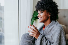 Happy Young Woman With Coffee Cup Sitting By Window At Home