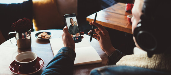 Wall Mural - Young man has video call conference with friend using his mobile phone. Working at cafe