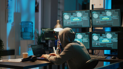 Impostor with mask hacking computer server late at night, working on laptop and multiple monitors to steal IT information. Mysterious masked thief with hidden identity doing cyber crime.