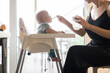 Mother spoon feeding her baby boy child in baby chair with fruit puree in kitchen at home. Baby solid food introduction concept
