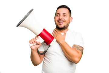 Canvas Print - Young caucasian man holding a megaphone isolated laughs out loudly keeping hand on chest.