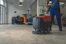 Cleaner Cleans Hard Floor With Scrubber Machine While Other Cleaner Cleans In The Background