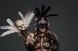 Shot of painted voodoo witch with staff dressed in fur and plumed headdress.