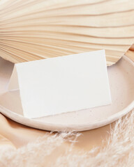 Wall Mural - Folded card near dried palm leaf and beige silky fabric close up, greeting or wedding mockup