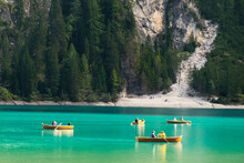 Tourists Ride Wooden Boats On Braies Lake With Transparent Water And Dolomites On The Background In Sunny Day.