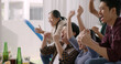 © ChayTee - Group of young adult friend man and woman asia people sit at sofa couch joy chanting party fun game FIFA world cup live TV at home eat snack bowl drink beer bottle glass jump mad happy win exult face.