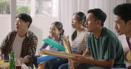 Wall Mural - Group of young adult friend man and woman asia people sit at sofa couch joy chanting party fun game FIFA world cup live TV at home eat snack bowl drink beer bottle glass jump mad happy win exult face.