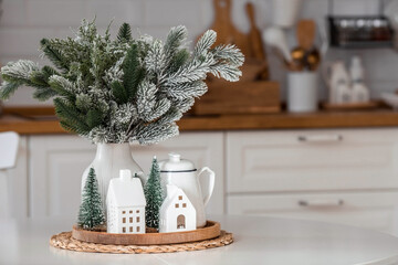 A spruce bouquet and Scandinavian houses on a white kitchen table. Christmas decorations in the interior. The concept of preparing for the New Year holiday.