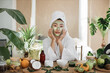 © sofiko14 - Portrait of beautiful young asian woman with green cosmetic mask on face and towel on head over exotic background. Pretty lady doing skin care procedures indoors at home.