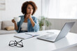 © LIGHTFIELD STUDIOS - laptop and stationery on desk near blurred african american freelancer with cup.