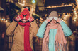 Photo of two positive carefree people arms covering eyes toothy smile evening lights outside