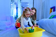 Child with physical disability in sensory stimulating room, snoezelen. Child living with cerebral palsy interacting with her therapist during therapy session.