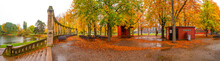 Panorama Over Lonely Empty Benches Under Old Chestnut Trees And Old Columns With Fallen Red And Orange Leaves In The City Park In Autumn Colors In Rainy Day, Magdeburg, Germany.