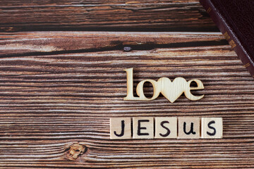 Wall Mural - Love Jesus text written with wooden cubes and letters with heart shape placed on rustic background with closed Holy Bible Book. Copy space. Top view. Christian biblical concept.