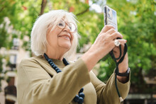 Cheerful Senior Woman Taking Self Portrait Standing Near Green Trees