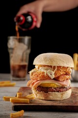 Canvas Print - Vertical shot of a hamburger with meat and sauces on a wooden board in a dark background