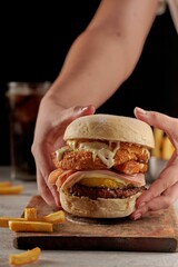 Canvas Print - Vertical shot of a hamburger with meat and sauces on a wooden board in a dark background