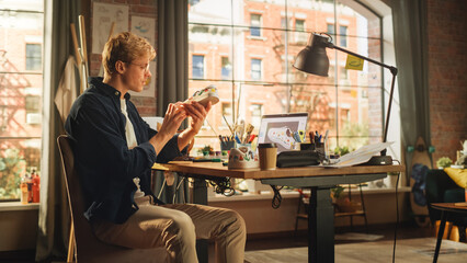 Leinwandbilder - Young Male Artist Working on Custom Made Sneakers in Front of his Laptop Computer in Creative Loft Office. Man Drawing on White Shoes. Trendy Design For Fashion Show Concept.