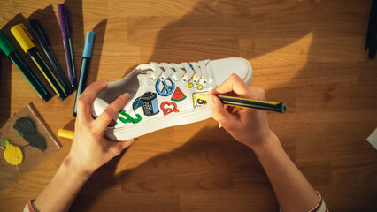 Leinwandbilder - Top View Shot: Designer Sitting Behind the Wooden Desk at Home and Applying Colourful Pictures on Shoes. Hand Made Stylish Footwear and Creative Process Concept. Close Up.