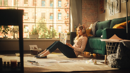 Poster - Young Pretty Woman with Blond Hair Wearing Headphones. Working from Home on Laptop Computer in Stylish Loft Apartment. Creative Female Sitting in Relaxed Pose and Checking Social Media.