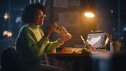 Leinwandbilder - Active Black Female Designer Sitting in the Evening in Loft Studio and Working on Shoes Customisation. Living Room with Big Window. Next Generation and Trendy Fashion Design Concept.