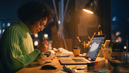 Leinwandbilder - Side View of Active Female Designer Sitting in the Evening in Loft Studio and Working on Shoes Customisation in Front of Her Laptop. Next Generation and Trendy Design Concept.