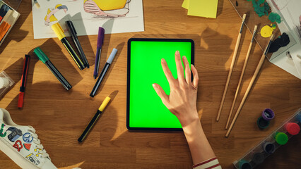 Leinwandbilder - Top View of Young Designer Sitting at the Desk and Working on Tablet Computer with Green Screen Chroma Key on Display. Creative People with Fresh Brave Ideas for Clothing Design Concept.